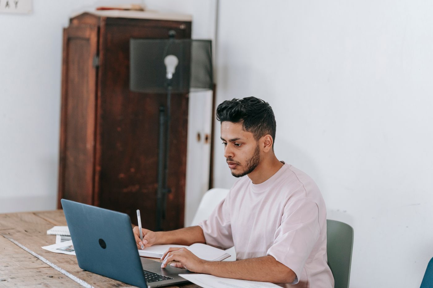 A young adult man writing thoughtful notes beside his laptop